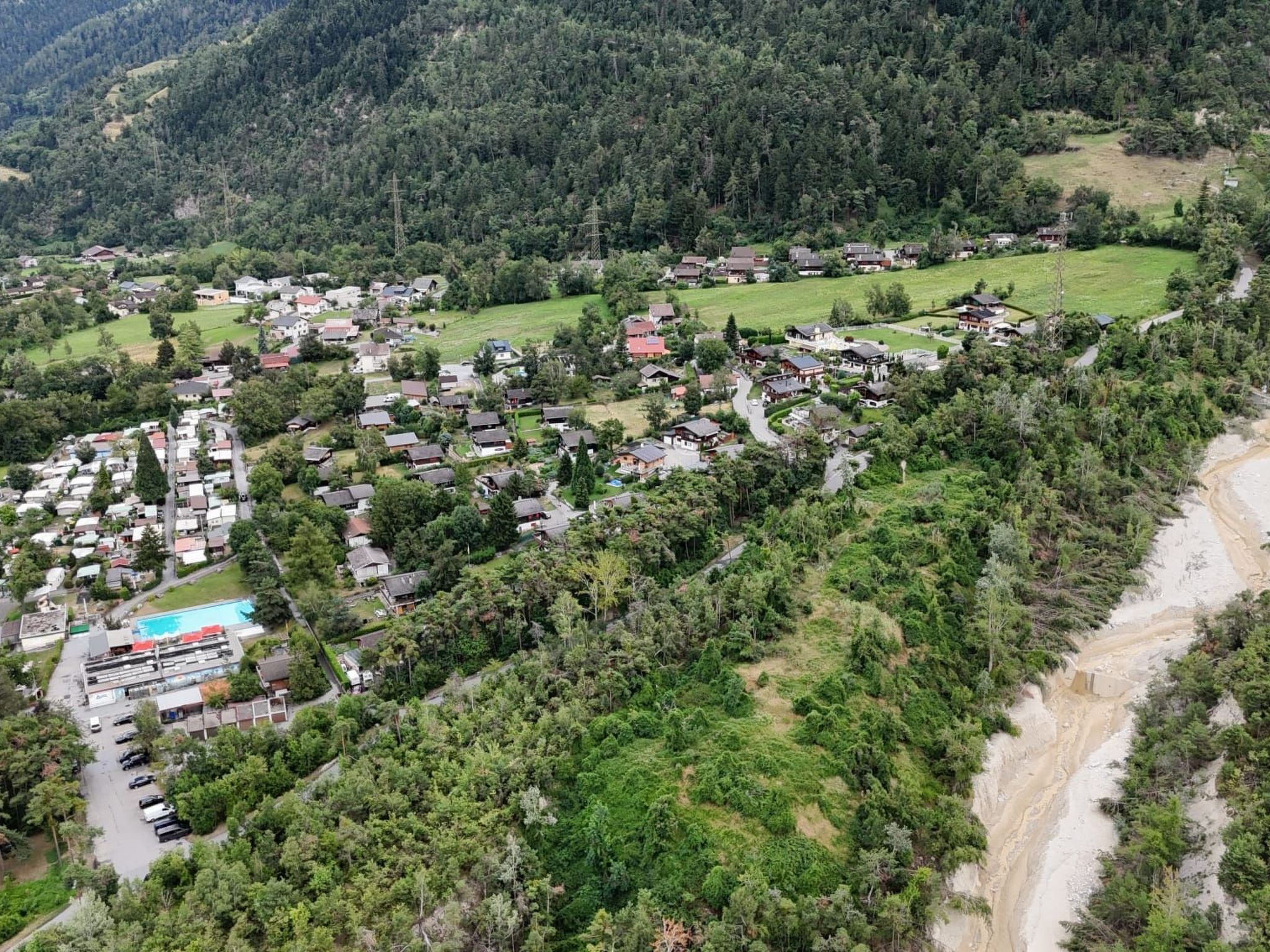 Vista aérea de una zona residencial con casas, una piscina y una ladera cubierta de bosque.