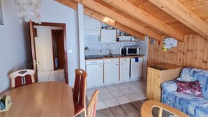 A cozy kitchen with white cabinets, a microwave, and a sink. There's a dining area with a wooden table and chairs, and a blue sofa with a cushion. - Chalet Haus (bei Einfahrt grosser Nussbaum ) by Interhome (Leuk-Susten)