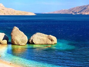 A clear view of a beach with large rocks in the water and a distant mountain range. - Wohnung "Rino" mit Blick auf das Wasser by Interhome (Pag/Pag)