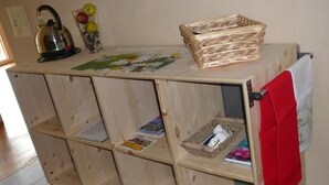 Een houten opbergkast met verschillende vakken, waarvan sommige een waterkoker, een mand en een rode handdoek bevatten.