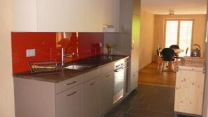 Een moderne keuken met een rode achterwand, roestvrijstalen apparatuur en een eethoek met een houten tafel en stoelen.