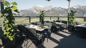 Eine Terrassensitzgruppe mit Tischen und Stühlen, Blumentöpfen und Blick auf die Berge.