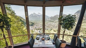 Ein Essbereich mit einem Tisch für zwei Personen, große Fenster mit Blick auf eine Stadt und Berge, sowie zwei Topfpflanzen.