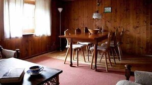 A wooden dining room with a table and chairs, a window with curtains, and a wooden ceiling.