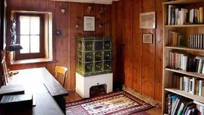 A room with wooden walls, a bookshelf, a desk with a lamp, and a window.