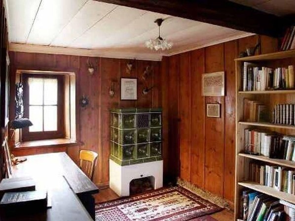 A room with wooden walls, a bookshelf, a desk with a lamp, and a window.