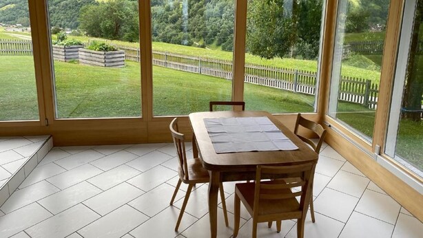 A dining area with a table and chairs, large windows with a view of a green landscape. - "Ferienwohnung ""Spel Rein"" Cumpadials" by Interhome (Cumpadials)