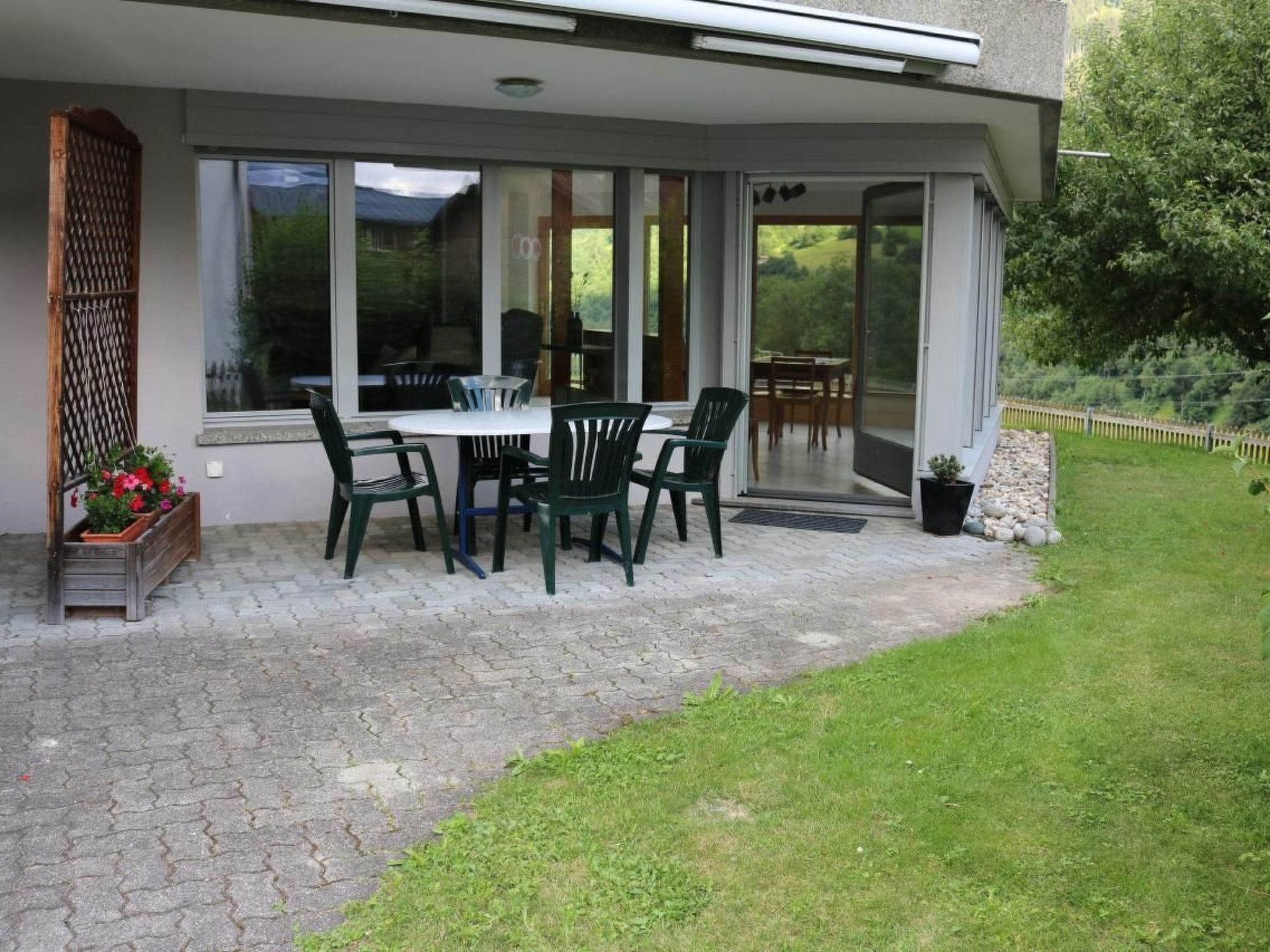 Une terrasse avec une table et des chaises, entourée de grandes fenêtres et offrant une vue sur l’extérieur.