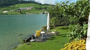 Un patio junto al lago con mesas al aire libre y vistas a un pueblo al otro lado del agua.