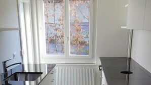 Una cocina moderna con armarios blancos, encimera negra y ventana con vistas a árboles.