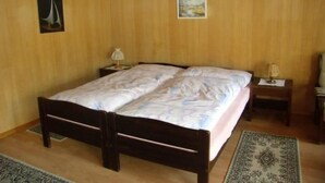 Een kamer met houten lambrisering, een tweepersoonsbed, twee nachtkastjes en een hanglamp.