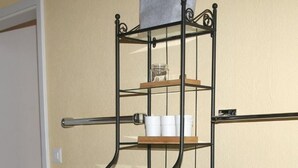 A metal multi-tiered shelf unit with various items on it, including folded towels and cups, against a beige wall. - Apartment Kat A by Interhome (Dürrenroth)