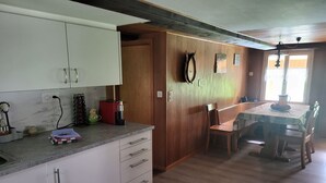 Een keuken met witte kasten, een eethoek met een houten tafel en een plafondventilator.