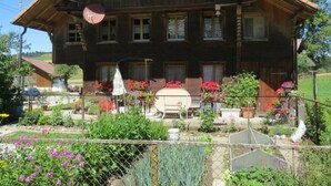 Een traditioneel houten huis met een pannendak, meerdere ramen en een verzorgde tuin met diverse planten en bloemen.