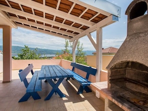 A covered patio with a wooden table and benches, a stone oven, and a scenic view. - Apartment  by Interhome (Krk/Šilo)