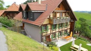 A traditional chalet with a sloped roof, a balcony with green shutters, and a small outdoor seating area with umbrellas. - Lamahof Tschäppel by Interhome (Huttwil)