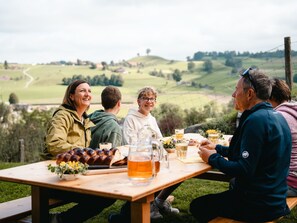 Un grupo de personas sentadas en una mesa de picnic de madera al aire libre, con vistas panorámicas de colinas ondulantes al fondo.