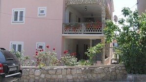 En toetages bygning med rosa facade, en stentrappeindgang og en balkon med røde blomster.