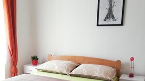 Una camera da letto ordinata con un letto in legno, biancheria verde e beige, una piccola pianta in vaso e una cornice con l'immagine della Torre Eiffel appesa al muro.