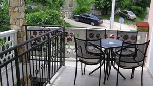 Un balcone con pavimento piastrellato, ringhiera in metallo e due sedie in rete attorno a un tavolino.