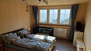 Une pièce en bois avec un lit, un bureau, une télévision et une fenêtre avec des rideaux.