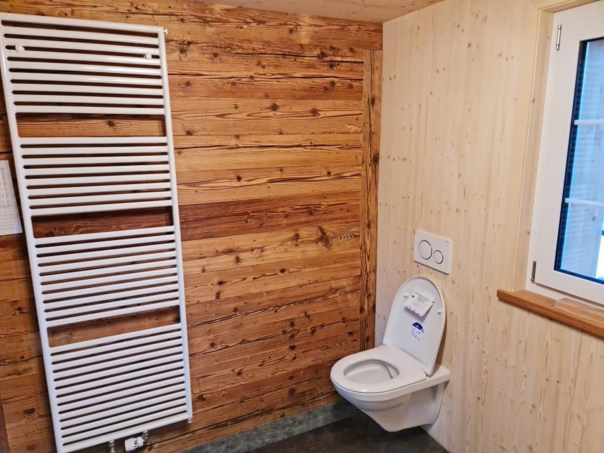Ein Badezimmer mit Holzwandverkleidung, einer Toilette und einer Lüftungsanlage.