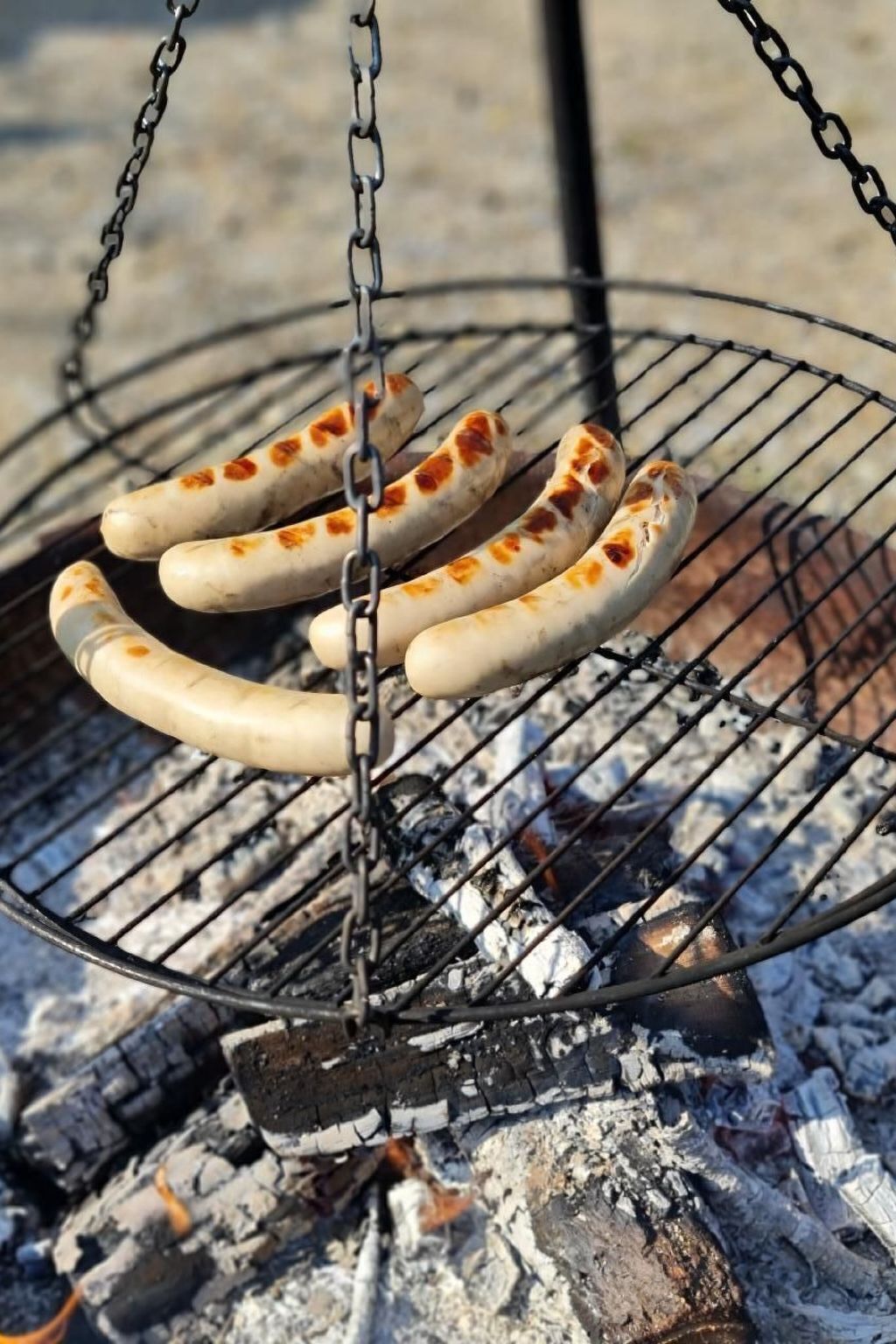 Sausages being grilled on a metal rack over an open fire.