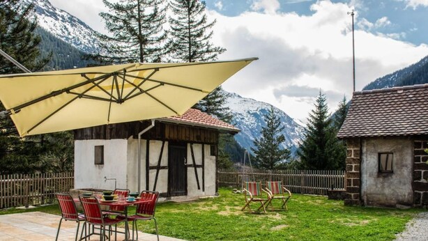 Une terrasse avec une table et des chaises, un parasol jaune et une vue sur les montagnes en arrière-plan.