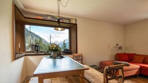 Un salon chaleureux avec une table à manger en bois, un canapé rouge et une vue sur les montagnes par une grande fenêtre.
