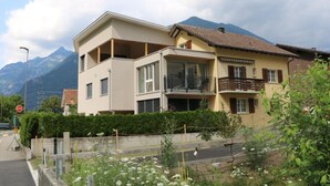 A two-story residential building with a balcony on the upper floor, surrounded by greenery and mountains in the background. - Ferienwohnung by Interhome (Attinghausen)