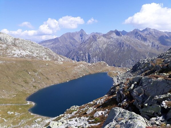 Paisaje montañoso con un lago azul cristalino rodeado de terreno rocoso y cumbres distantes.