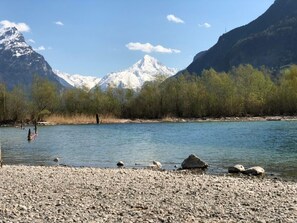 Un río con orilla rocosa y montañas nevadas al fondo.