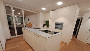 A modern kitchen with a central island, built-in appliances, and a sliding glass door leading to a dining area. - Ferienwohnung by Interhome (Attinghausen)