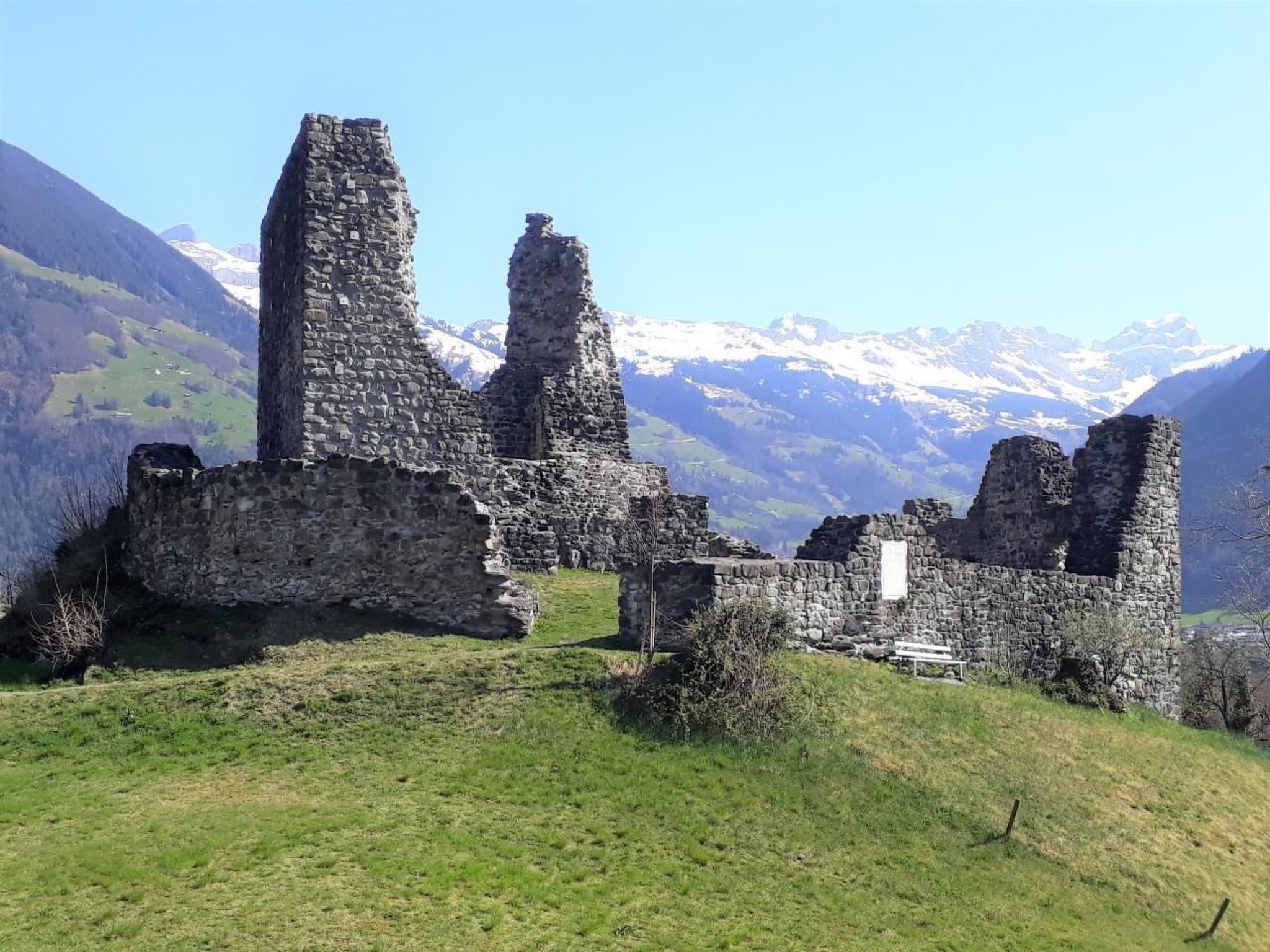 The ruins of a stone building with a grassy foreground and a mountainous backdrop.