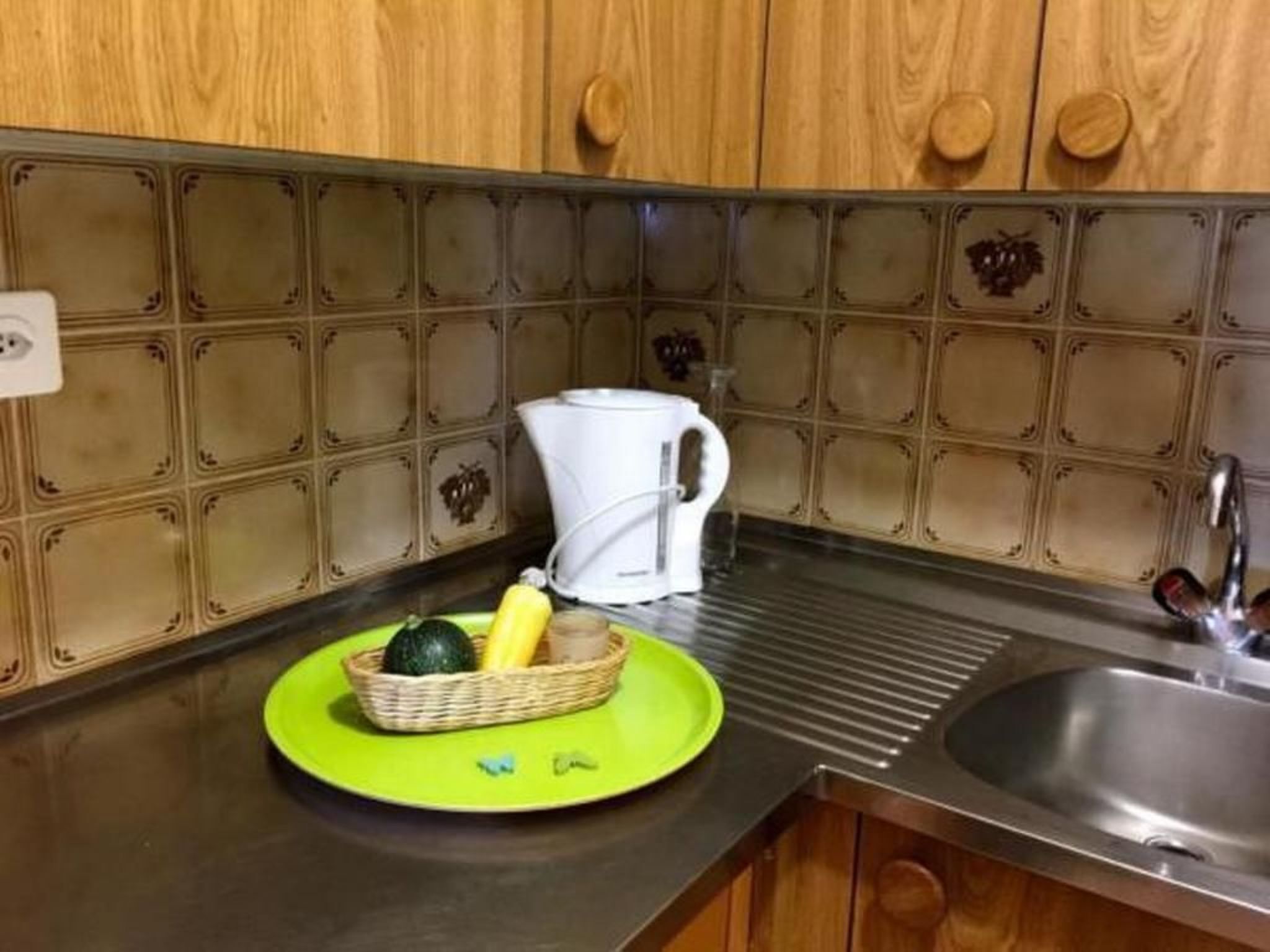 A kitchen with wooden cabinets, a stainless steel sink, and a green cutting board with vegetables.