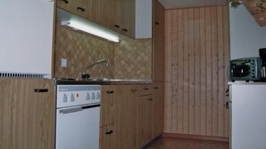 A compact kitchen with wooden cabinets, a white refrigerator, a stove, and a microwave. - Fruehalp by Interhome (Unterägeri)