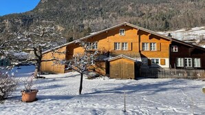 Un chalet en bois doté d’un balcon, entouré d’un paysage enneigé et surplombant un décor montagneux.