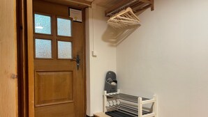 Une porte en bois avec un vitrage dépoli, un mur blanc, un paillasson noir à l’entrée, et un porte-manteau avec des cintres et un meuble à chaussures.