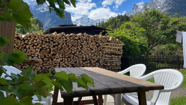 Une table et des chaises en bois, installées dans un jardin avec une montagne en toile de fond.