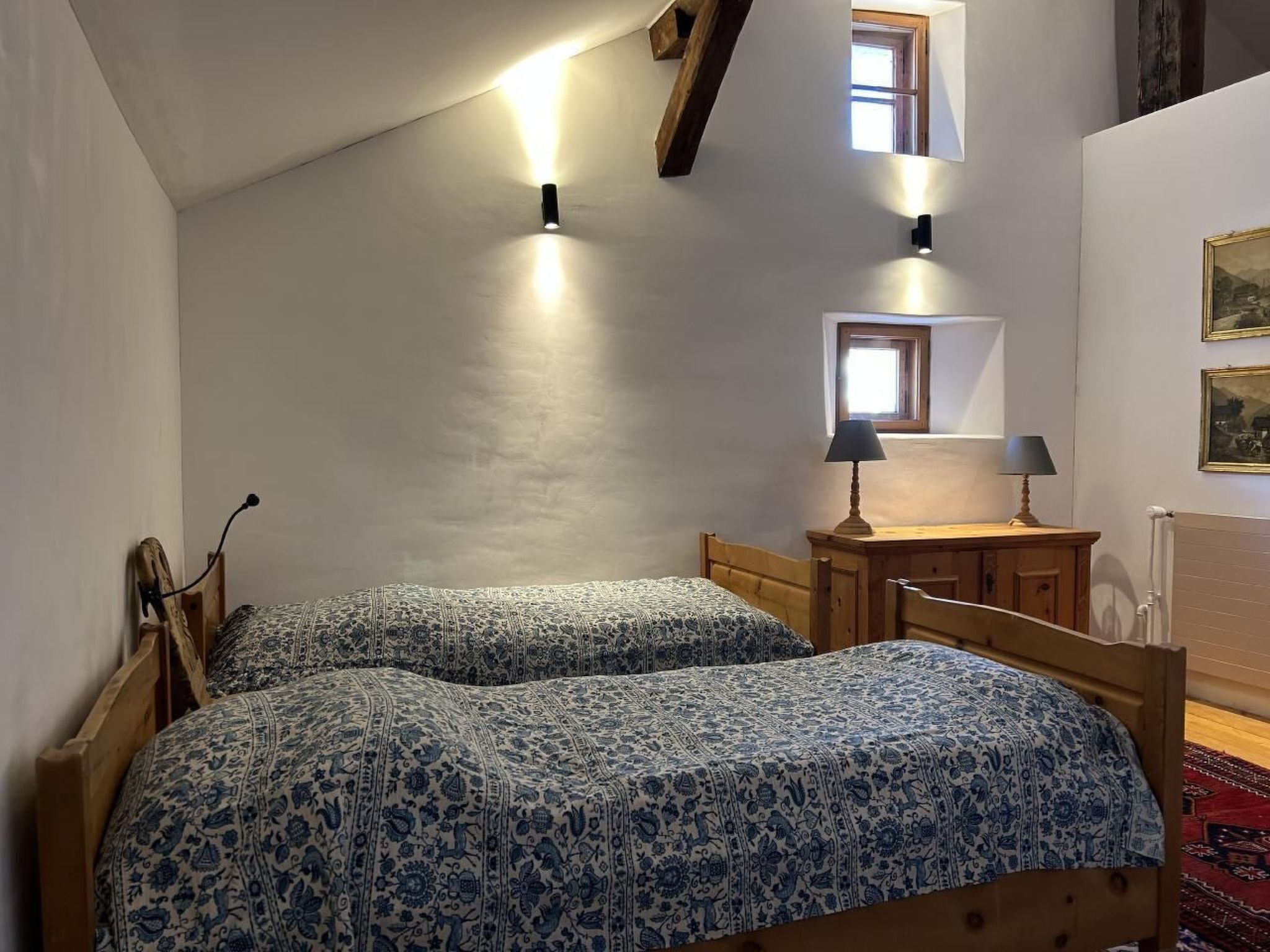 A bedroom with two wooden beds, a desk, two wall-mounted lamps, and a radiator.