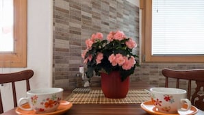 A dining table with two floral cups and saucers, a red pot with pink flowers, and a checkered placemat. - mit Blick auf das Wasser by Interhome (Trogir)