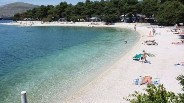 A beach with clear turquoise water, white sand, and a line of trees in the background. - mit Blick auf das Wasser by Interhome (Trogir)