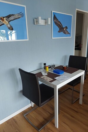 Un comedor con una mesa blanca, sillas negras y dos cuadros enmarcados de pájaros en la pared.
