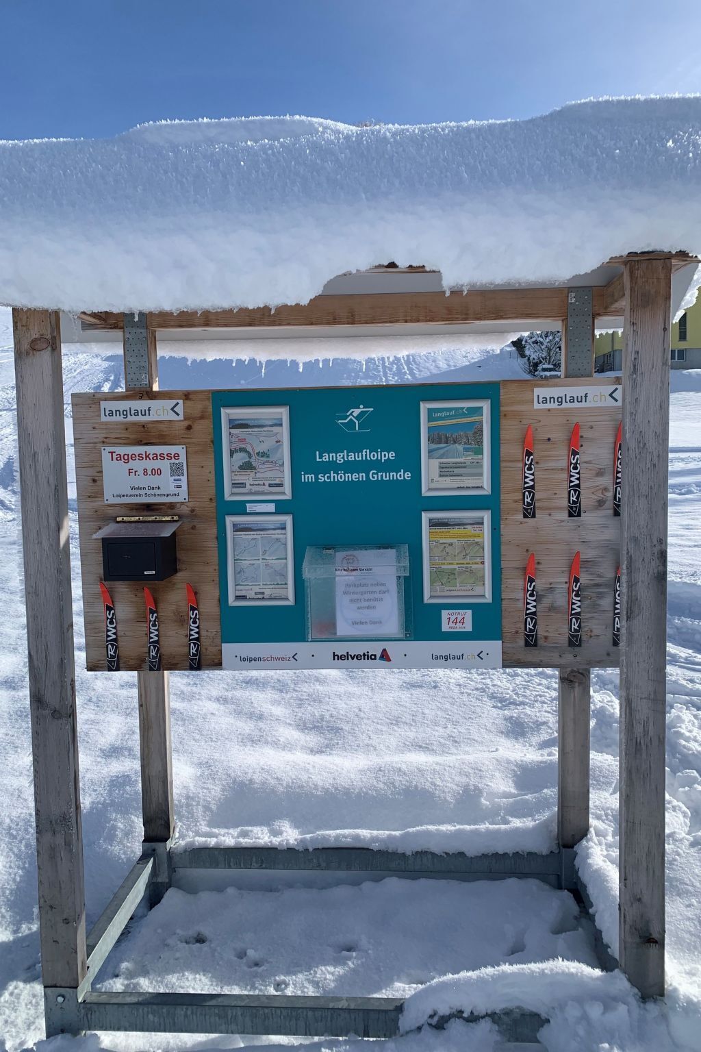 Un panel informativo de madera con señales direccionales y un código QR, sobre un paisaje nevado.