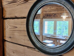 Pared de madera con un espejo circular que refleja una habitación con una mesa y sillas.