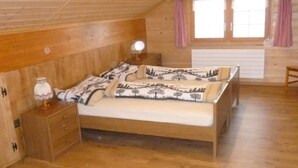 Et soveværelse med træloft, seng med mønstret sengetøj, et natbord med en lampe og et vindue med gardiner.