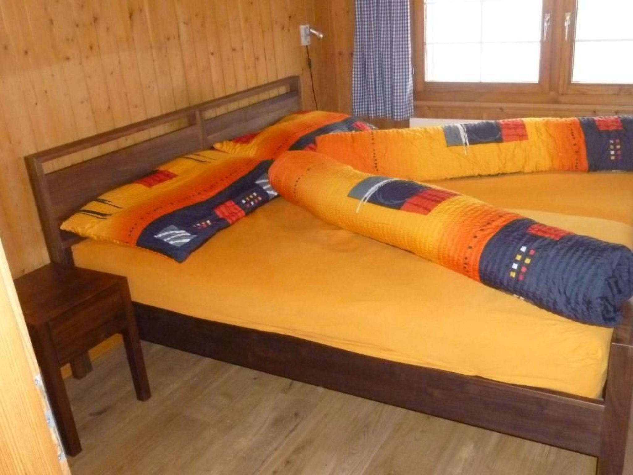 Una cama de madera con colchón amarillo y almohadas de diseño azul y naranja.