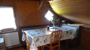 Et hyggeligt interiør i en hytte med et træbord dækket af en blomstret dug, omgivet af træstole.