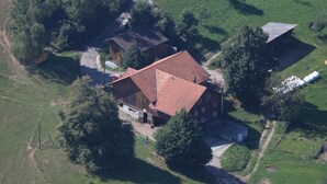 Vue aérienne d’une maison de campagne avec un toit rouge, entourée de verdure et bordée d’un chemin de terre.