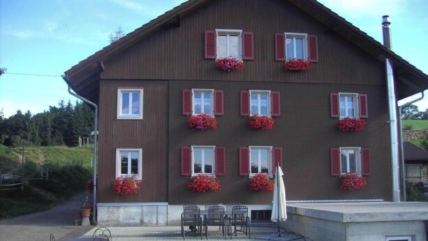 Un immeuble de deux étages avec des volets rouges et des jardinières aux fenêtres.